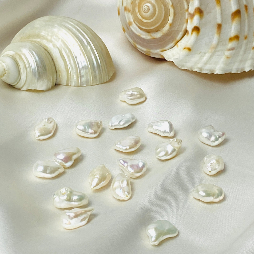 Lose Keshi-Perlen auf einem seidigen Untergrund mit zwei Muscheln im Hintergrund