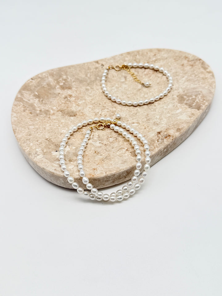 Sina Perlenarmband und Halskette aus naturweißen Süßwasserperlen mit 14k Gold Filled Verschluss auf Marmorplatte arrangiert