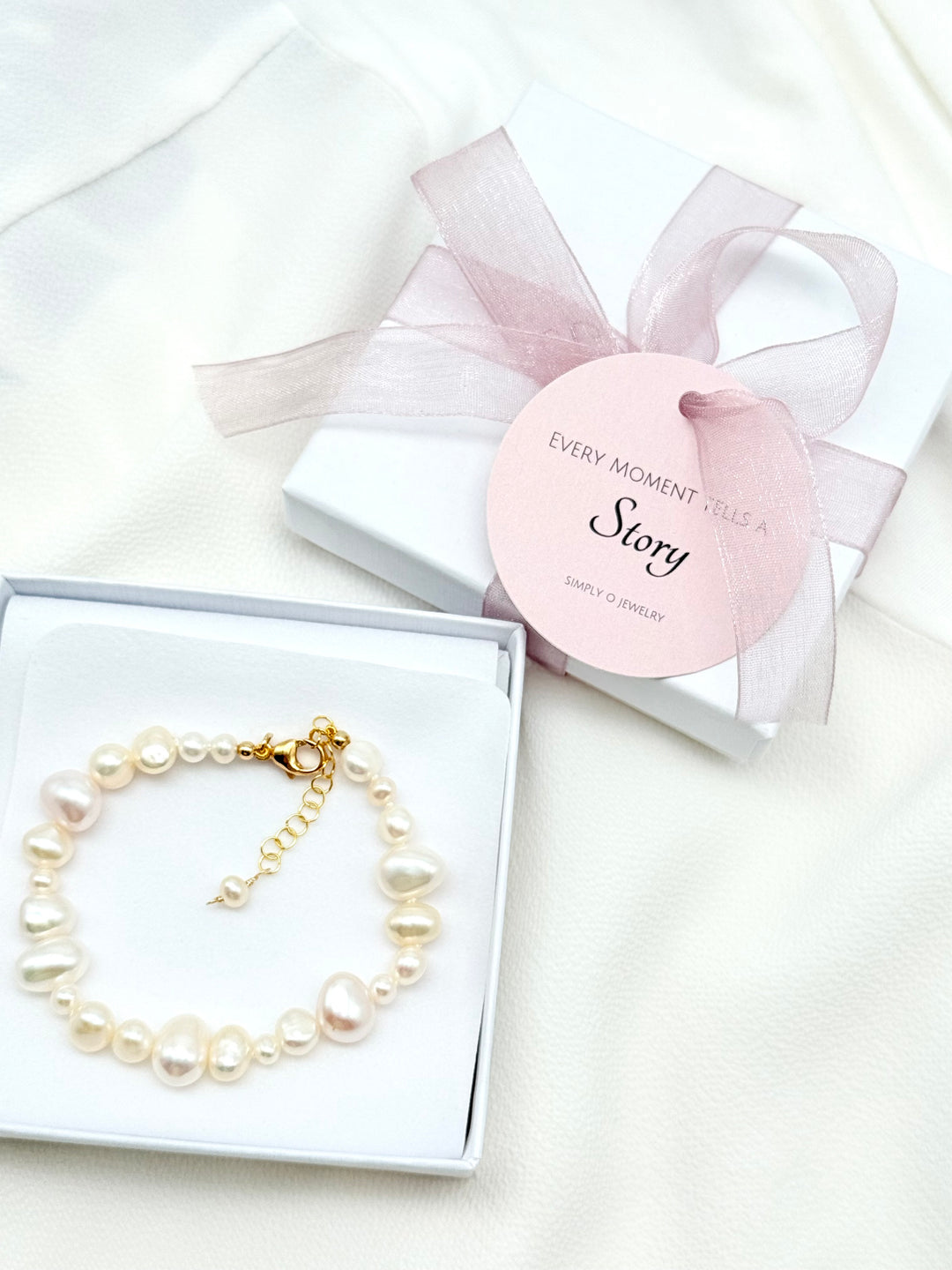 Louanne Perlenarmband aus weißen Süßwasserperlen in einer Simply O Schmuckbox, daneben eine Geschenkverpackung mit roséfarbener Organzaschleife.